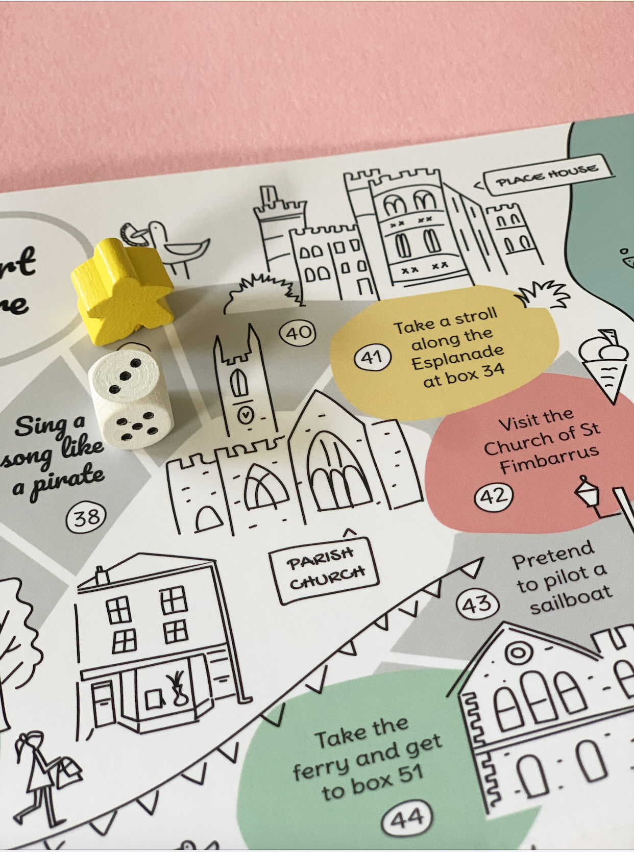 Fowey board game map detail with wooden dice and yellow marker, featuring the Place House and St Fimbarrus Parish Church.