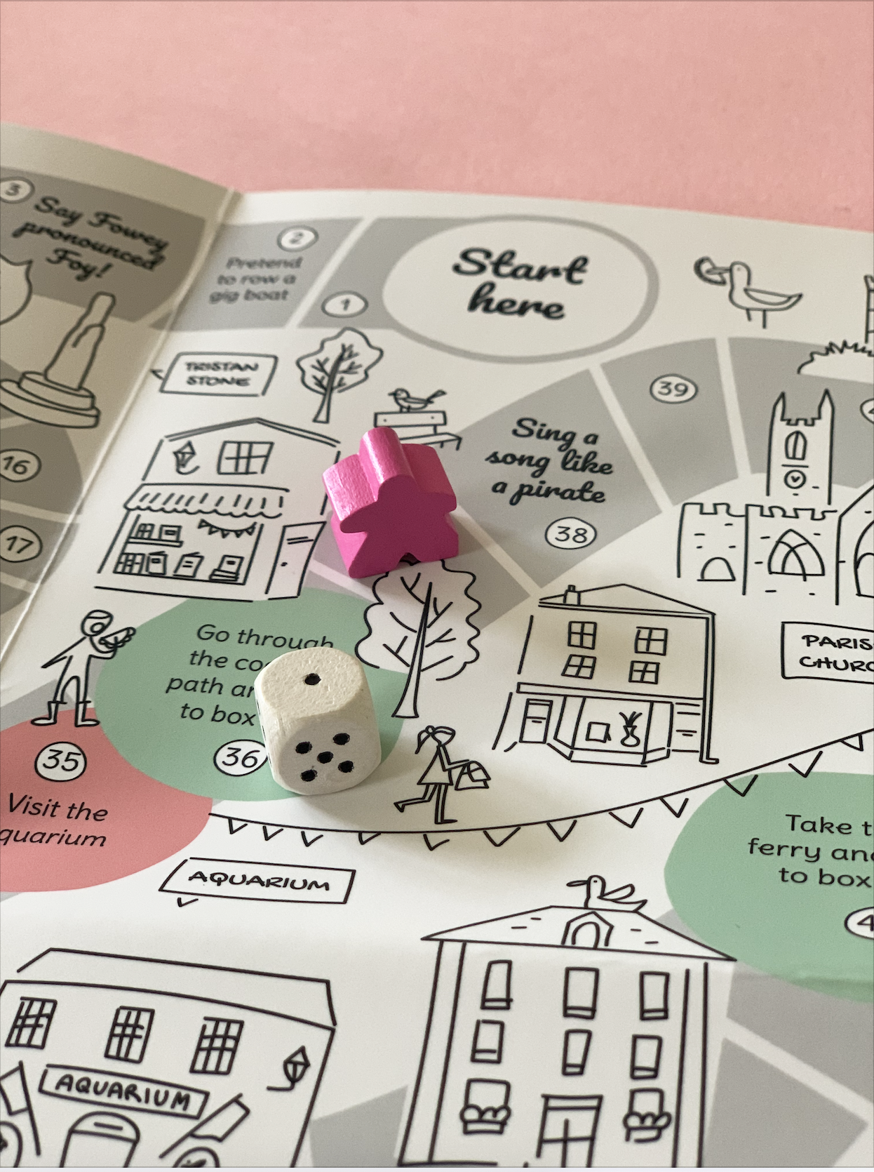 Fowey board game map detail with wooden dice and pink marker, featuring the Aquarium and Fimbarrus Parish Church.